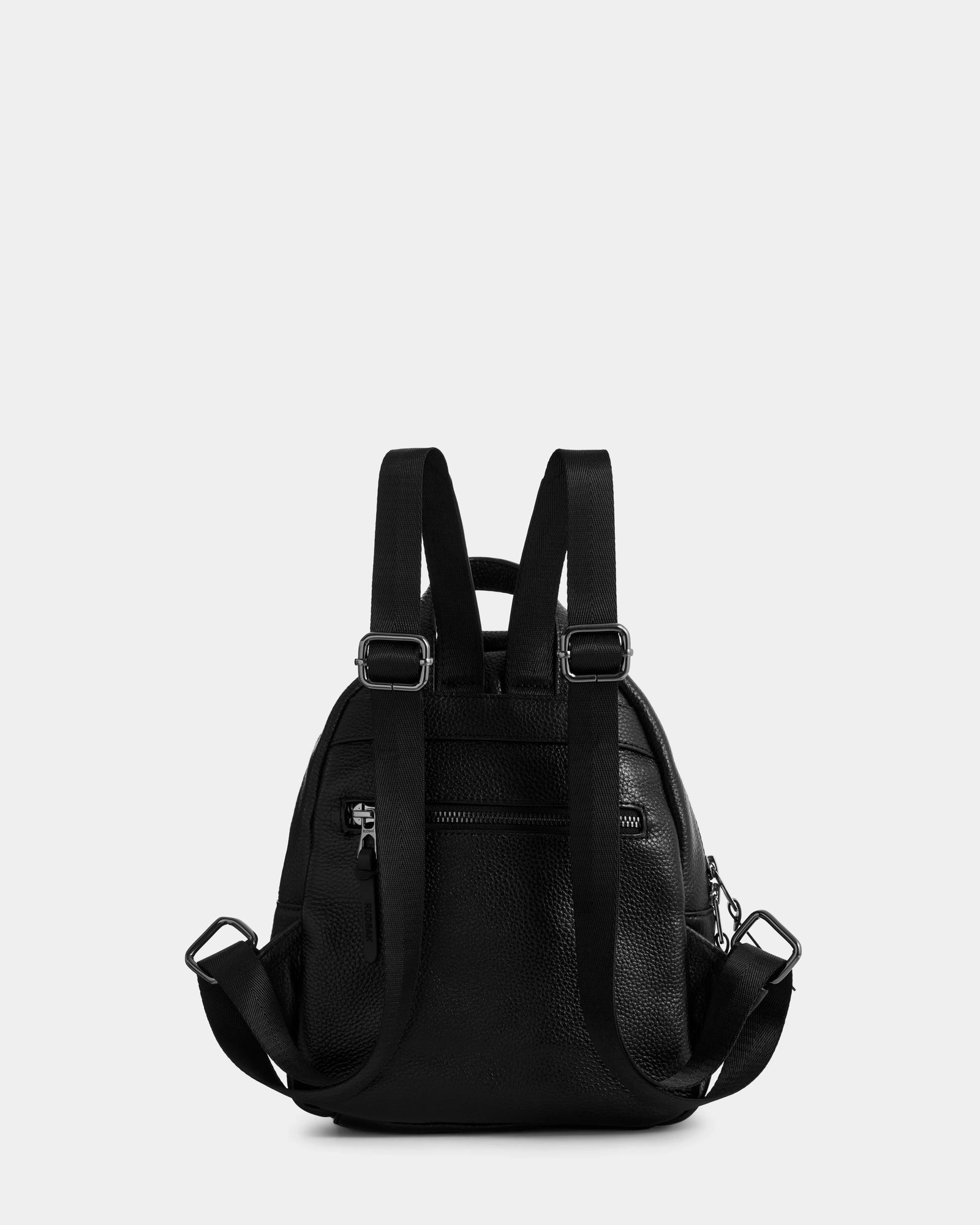 The Rudsak KATTY - L325014 Black mini backpack is shown from the back in black pebbled leather, featuring adjustable shoulder straps, a rear zip pocket, and silver hardware against a plain light grey background.