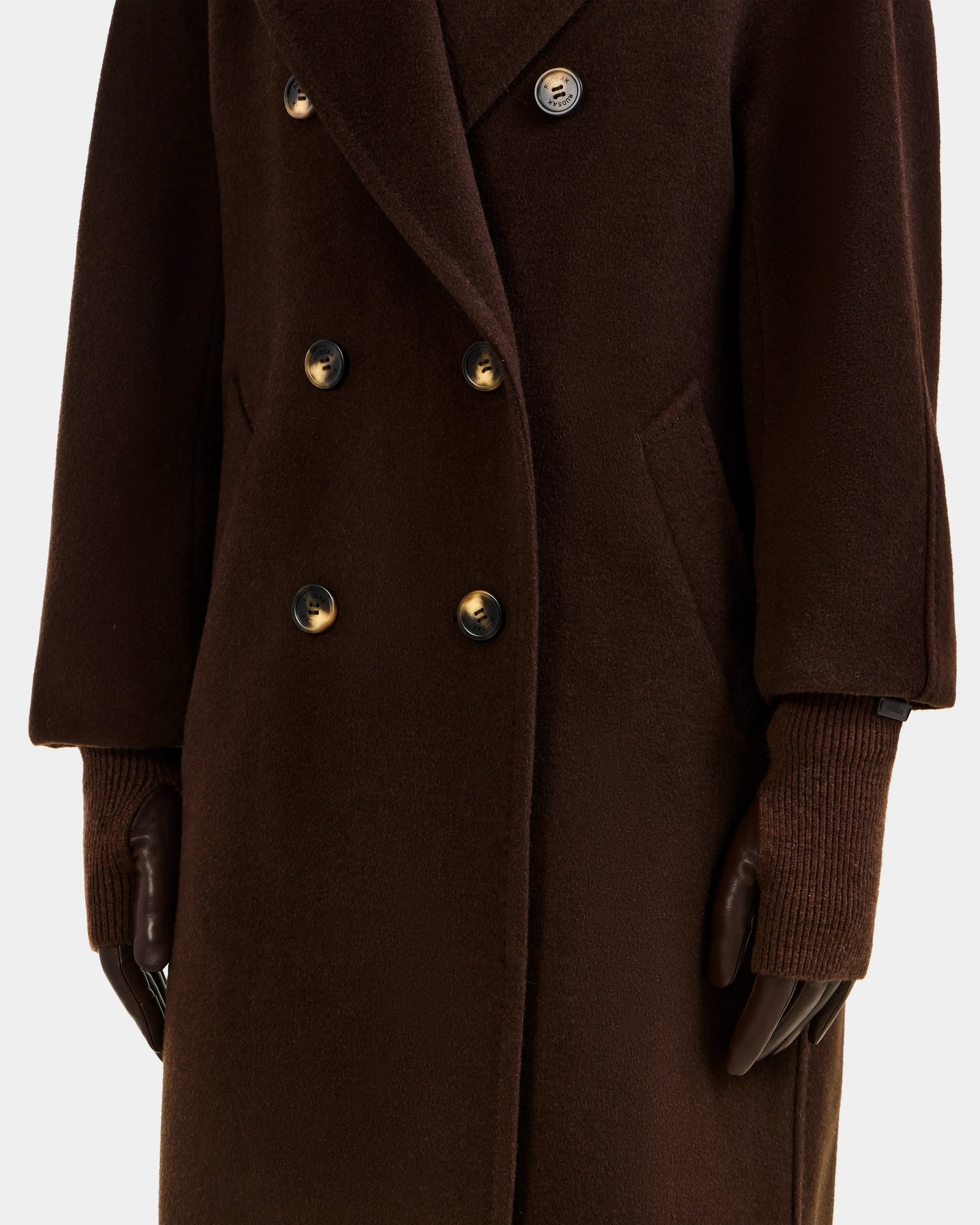A person wears the MARINE - 8424516 Espresso long double-breasted coat with ribbed knit cuffs, paired with dark brown Rudsak gloves. The image focuses on the torso and arms.