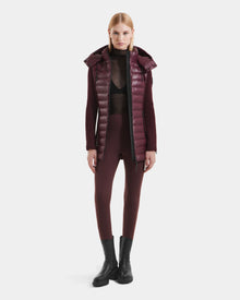 A woman stands facing forward wearing the Rudsak MARRY S - L125521 Wine weather-resistant puffer vest, a sheer black top, burgundy fitted pants, and black ankle boots against a plain white background.