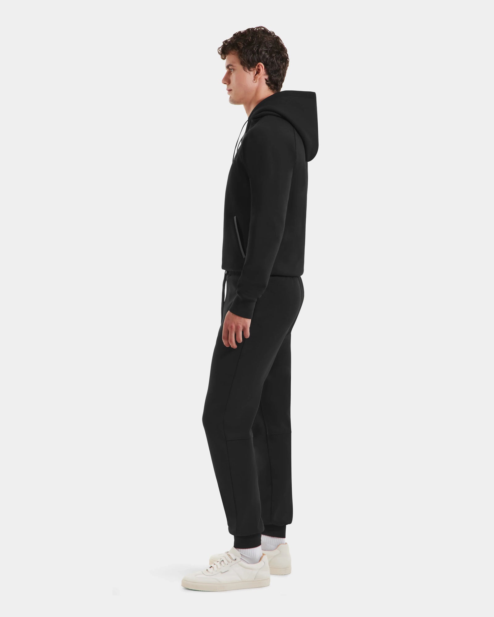 A man in profile faces left, wearing the Rudsak MAXTON - U525007 Black M hoodie and joggers for everyday comfort, with white sneakers, set against a plain white background.