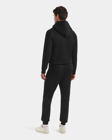A person faces away, wearing the Rudsak MAXTON - U525007 Black M hoodie and unisex jogger pants with white sneakers, set against a plain light background.