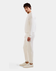 A man stands sideways facing left, wearing the Rudsak MAXTON - U525007 Vanilla M cotton-blend jogger, sweatshirt, and white sneakers against a plain white background for effortless everyday comfort.