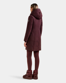 A person stands facing away, wearing the Rudsak SARINA - L125550 Bordeaux women's down parka with a hood, maroon leggings, and maroon winter boots against a plain white background.
