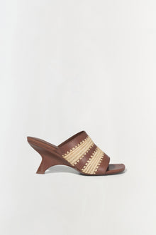 Brown leather mule sandal with woven raffia striped detailing across the upper and curved wedge heel.