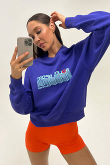 Model wears a royal blue crewneck sweatshirt with the lettering 