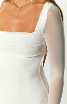 Close-up of the white dress showing the square neckline, ruched bodice, sheer mesh long sleeve, and side cutout