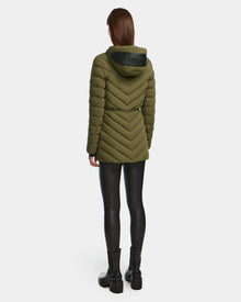 A person faces away, wearing the Rudsak FRANCINE - 8124722 Loden Green quilted puffer hooded jacket with RDS-certified down, black leggings, and black boots against a plain white background.