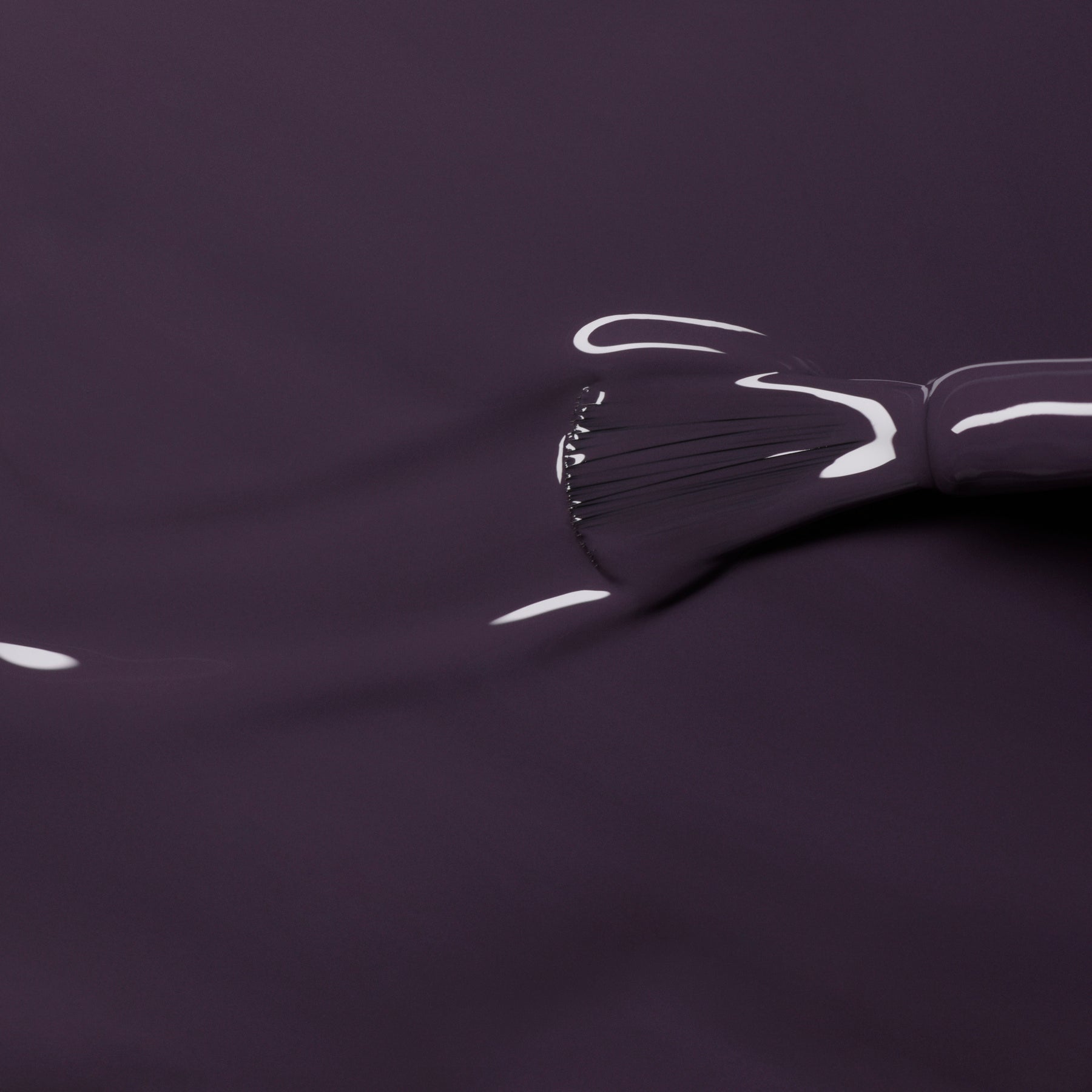 A close-up of the Manucurist Queen of Night brush applying glossy dark violet gel polish with gray undertones, reflecting light and enhancing depth on a smooth surface.