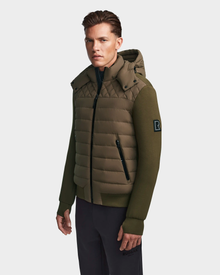 A man wearing the Rudsak LAURENZO - M123514 Light Olive jacket with a quilted front, ribbed cuffs, and black zippered pockets stands against a plain white background.