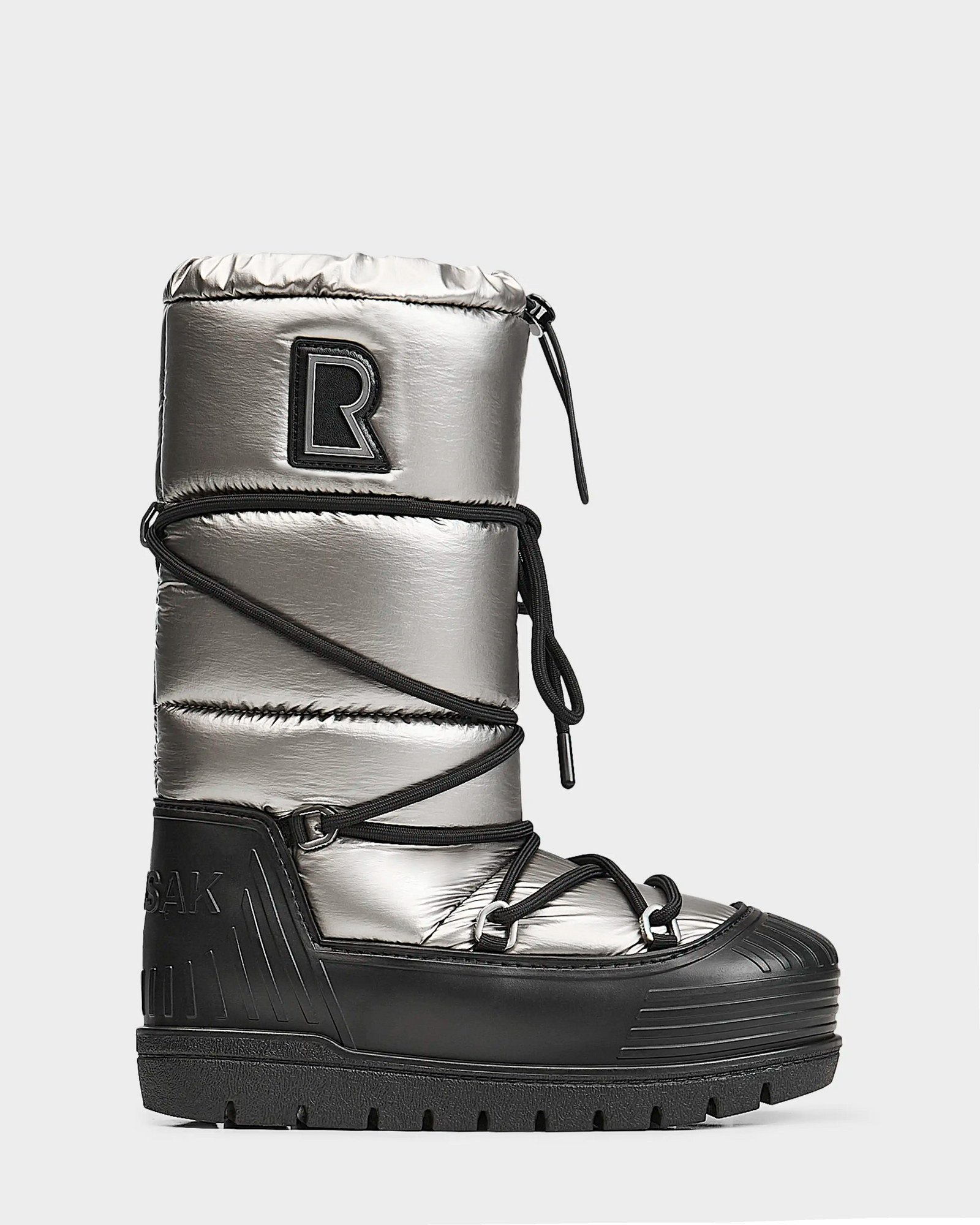 The Rudsak TISH - L223508 Pewter is a womens high-top winter boot with a shiny silver upper, black platform sole, crisscross laces, quilted design, bold R patch near the top, and a chunky ridged sole for extra traction.