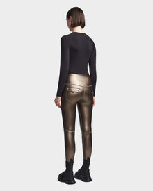 A person with short brown hair faces away, wearing a black long-sleeve top, Rudsak SIEN P - 8523027 METALLIC CHOCOLATE stretch vegan leather cargo leggings with pockets, and black chunky sneakers against a plain light background.