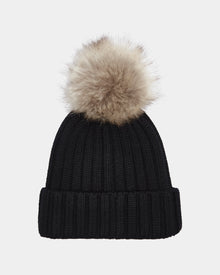 The Rudsak ANISA - L423500 Black/Natural is a black ribbed knit beanie with a folded brim and a large faux fur pom pom, perfect for upgrading your winter style. Shown against a plain light background.