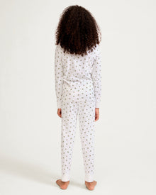 Kid's Pima Snug Fit Pajama Set in Mistletoe Moments: a two-piece white pajama set for children with a long-sleeve top, pants, green and red holly pattern, red scalloped neckline, and a red bow at the collar.