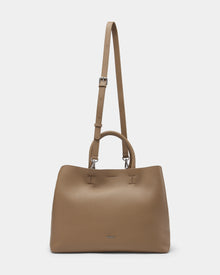 The CATIRA L - 8325007 Almond by Rudsak is a taupe women’s leather tote with double handles, a long adjustable strap, and a minimalist design featuring a small metallic logo—perfect as a versatile statement accessory.