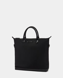 The Rudsak DEXTER - 9324513 Black is a minimalistic black canvas tote bag with two short handles and a zipper closure, showcased against a plain light gray background.