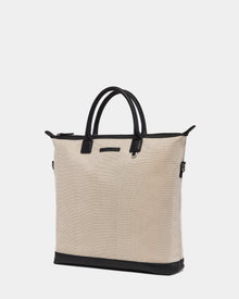 The Rudsak DEXTER - 9324513 Vanilla is a unisex beige canvas tote bag with black leather handles, trim, and base. Featuring a simple, structured design, its shown against a plain white background.