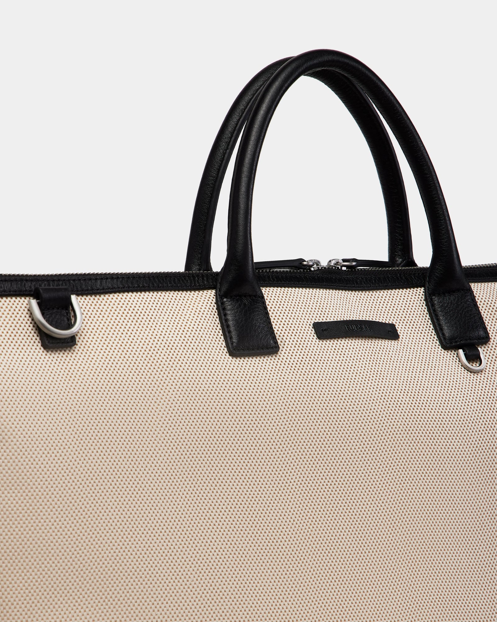 A close-up of the Rudsak DUBLIN - 9324514 Vanilla tote, a beige canvas leather weekender with black handles and silver hardware, set against a plain light gray background.