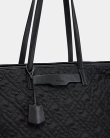 Close-up of the Rudsak LIVORNO - L325007 Black quilted monogram tote with embossed patterns, two long handles, a small leather tag, and a subtle brand name embossed on a leather strip near the top.