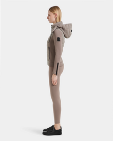 A woman stands in profile wearing the Rudsak MABS - 8124825 Cement fitted jacket with matching leggings and black sneakers, set against a plain white background.