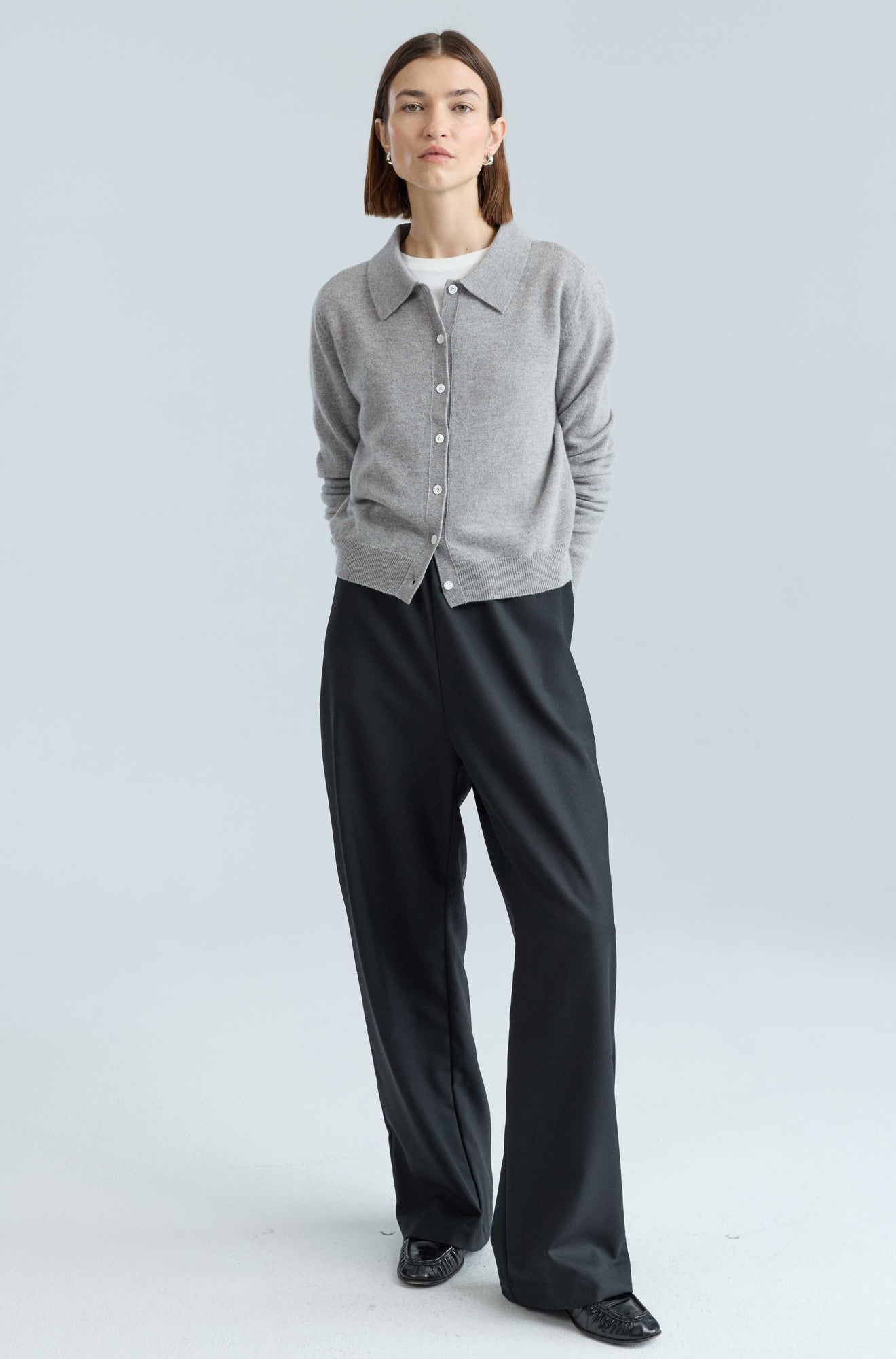 Person wearing a gray cardigan and black pants on a light gray background