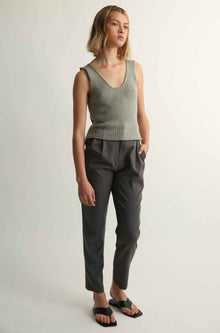 Woman wearing a green ribbed tank top and dark pants on a plain background