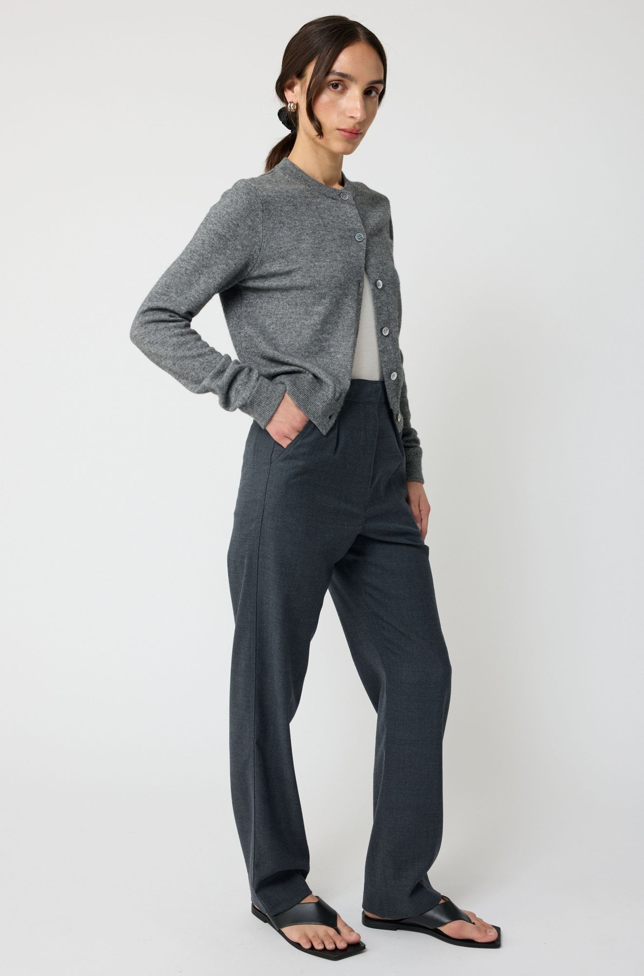 Woman wearing a gray cardigan and dark pants on a white background