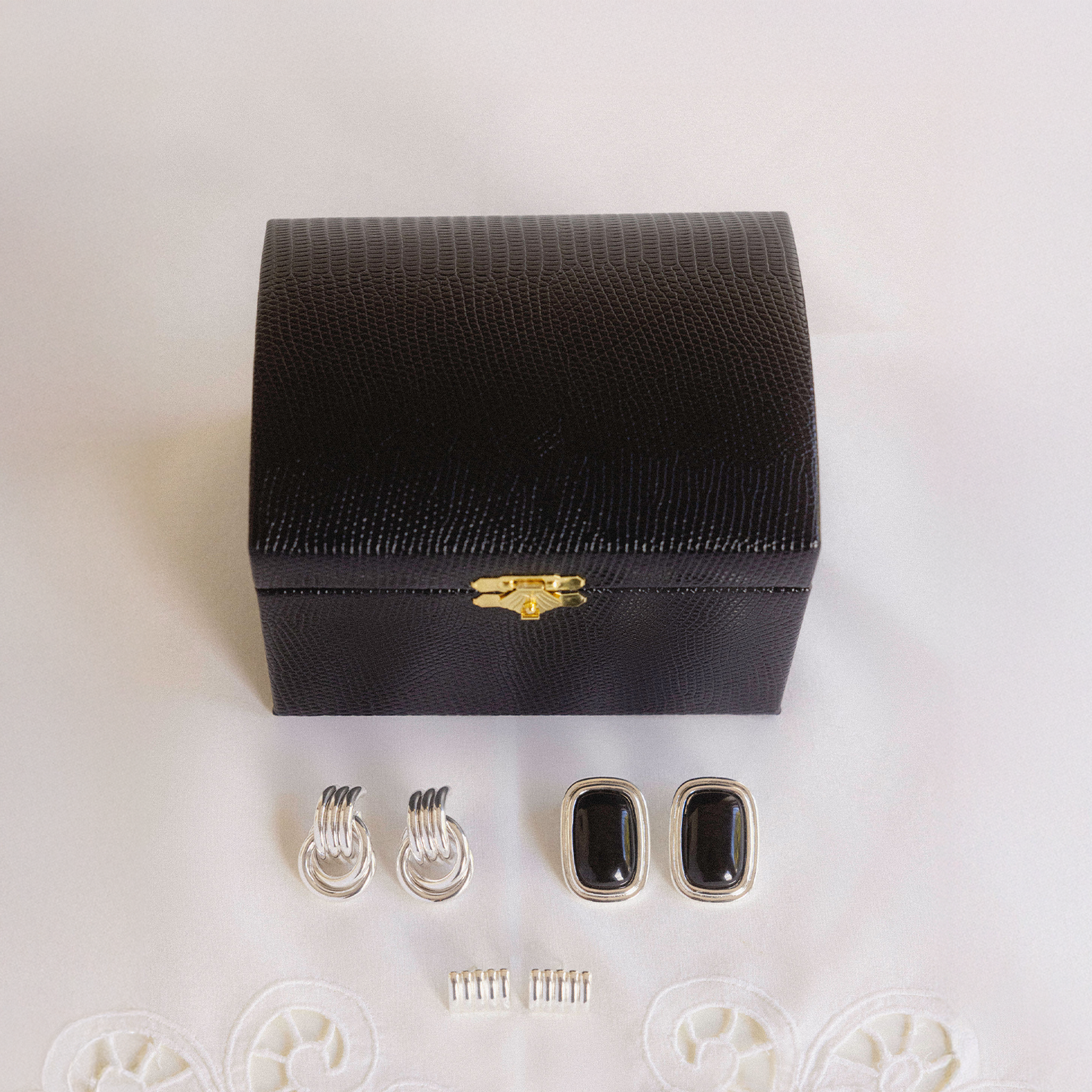 Black jewelry box with gold clasp, black earrings, and silver rings on a white background