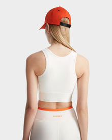 A woman wearing the Rudsak TRACY - 8524016 Eggshell racer-back sports bra and an orange cap.