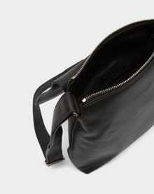 The Rudsak MADDY - 8322512 BLACK crossbody bag features black leather, a silver zipper, an open main compartment with a dark fabric interior, and an adjustable strap—ideal for minimalist style lovers.