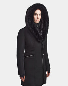 A woman wearing the Rudsak CORA - L123538 Black women’s fitted parka with a large fur-lined hood stands facing forward against a plain white background.