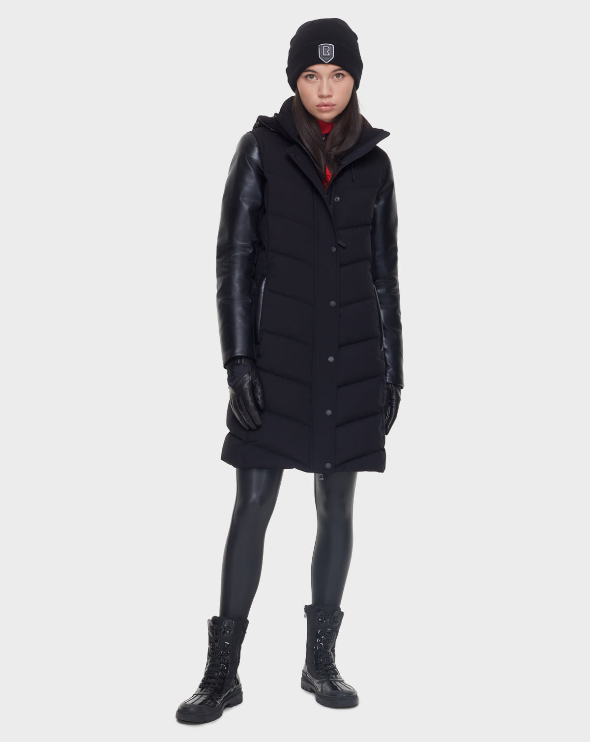 A woman stands confidently in the Rudsak ELSA - L121519 BLACK, a sleek, quilted down puffer that exudes timeless style and cozy sophistication.