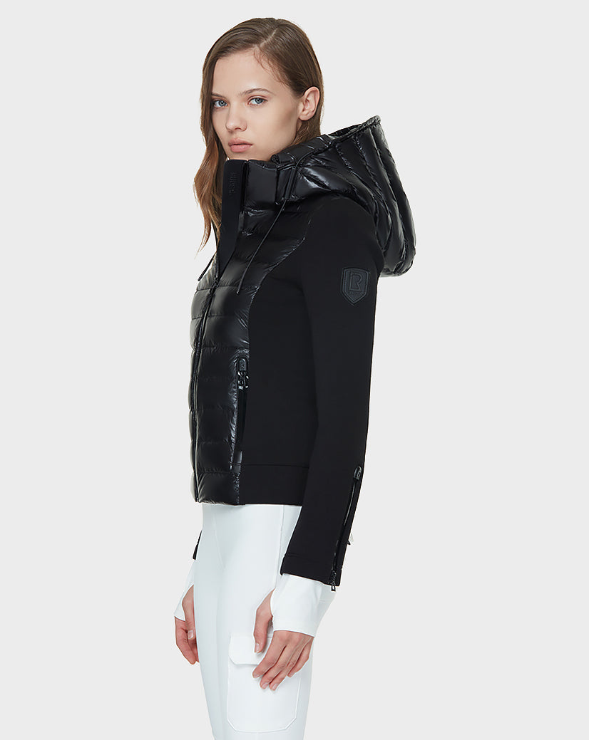 A woman faces sideways in a Rudsak MABS - 8121012 BLACK lightweight activewear jacket with waterproof zippers and hood, paired with white pants against a plain light gray background.