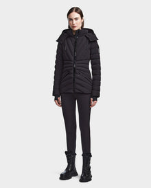 A woman faces forward in the Rudsak HANNA - 8123562 Black fitted winter down jacket with hood, made from SMART STRETCH fabric, styled with black leggings and lace-up boots against a plain light background.