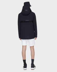 A person wearing the RUDSAK JACY - 6122000 BLACK trench, with a black bucket hat, white shorts, black socks, and black sneakers stands facing away against a plain white background.