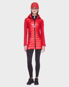 A woman faces forward wearing the Rudsak MERINA - 8121006 POPPY RED quilted down jacket with black accents, black leggings, sneakers, and a red baseball cap against a plain white background.